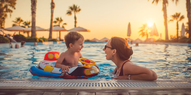 A Cute Little Boy Sitting In Pool Float & Busy Chatting With His Mom In The Pool.