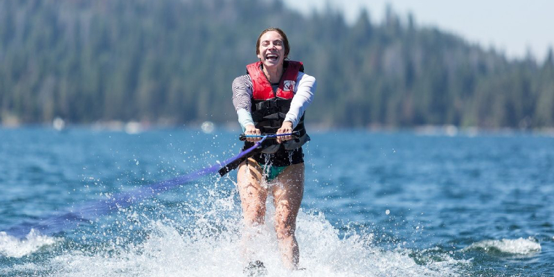 A Young Female Waterskier moving slow in splashes of water at a sunny day.