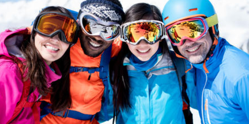 Two pair of couples in their winter suit standing in snow with their sport goggles