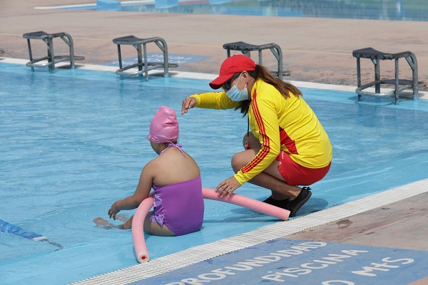 A Swimming coach is giving instructions to a girl in swimming costume sitting with her feet in water.